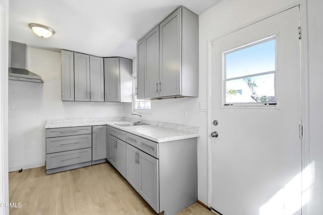 kitchen featuring wall chimney exhaust hood, gray cabinets, light countertops, and a sink