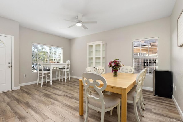 dining space with light wood finished floors, a ceiling fan, and baseboards