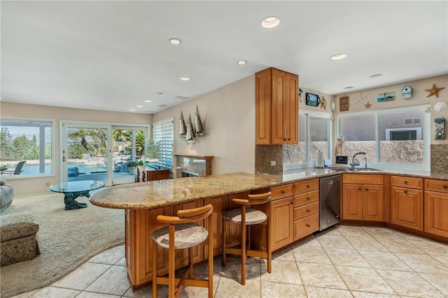 kitchen featuring light stone counters, a breakfast bar area, a peninsula, a sink, and dishwasher