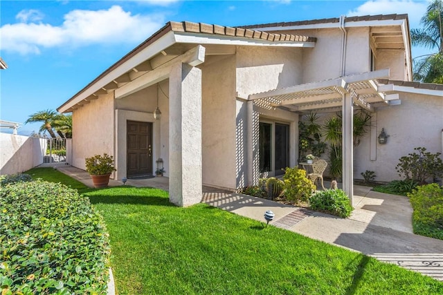 view of exterior entry featuring a patio, a yard, a pergola, and stucco siding