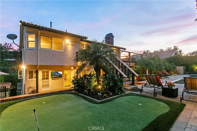 back of property at dusk featuring stucco siding, a chimney, and a patio