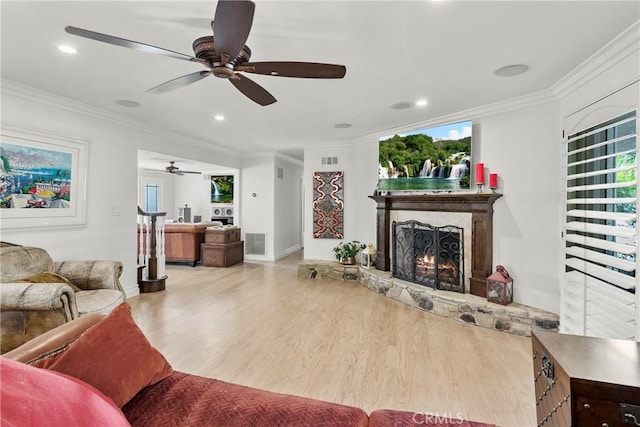 living area with a warm lit fireplace, visible vents, crown molding, and light wood-style flooring