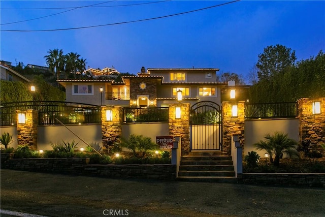 mediterranean / spanish-style home featuring stone siding, a fenced front yard, a gate, and stucco siding