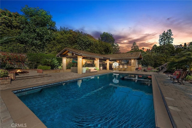 pool at dusk featuring a patio area and an outdoor pool