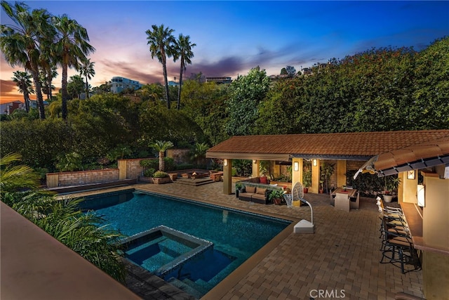 view of swimming pool featuring a pool with connected hot tub, an outdoor living space with a fire pit, and a patio area