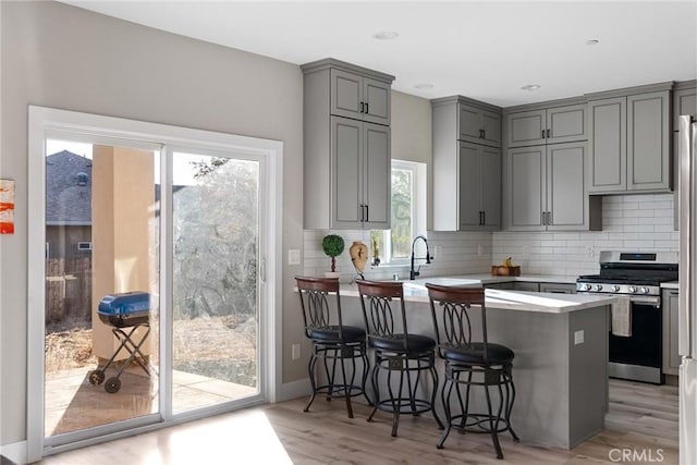 kitchen with a breakfast bar, a peninsula, stainless steel gas range, gray cabinets, and light countertops