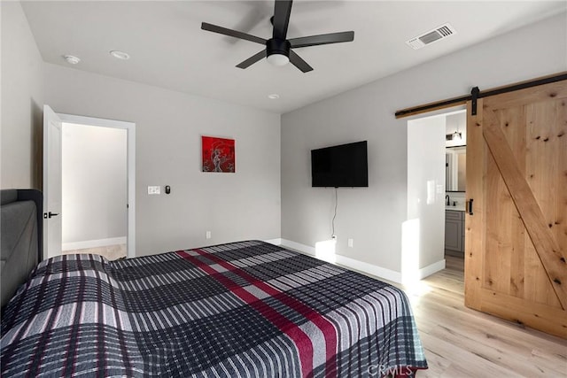 bedroom with ceiling fan, a barn door, visible vents, baseboards, and light wood-type flooring