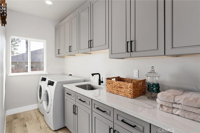 clothes washing area with cabinet space, light wood-style floors, a sink, separate washer and dryer, and baseboards