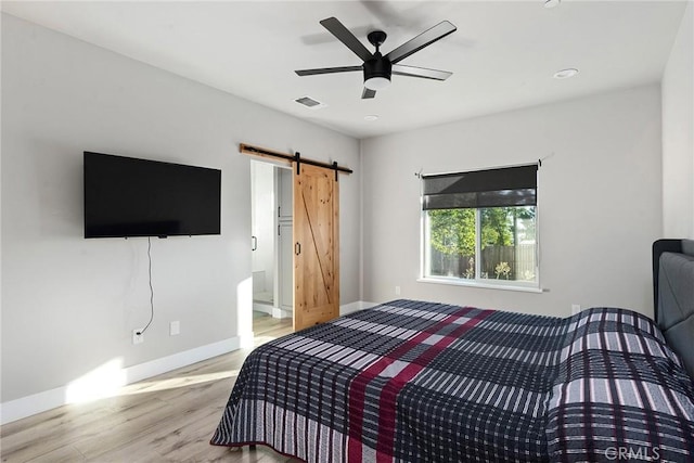 bedroom with a barn door, visible vents, baseboards, a ceiling fan, and light wood-type flooring