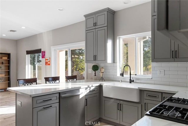 kitchen with gray cabinetry, a peninsula, a sink, dishwasher, and plenty of natural light