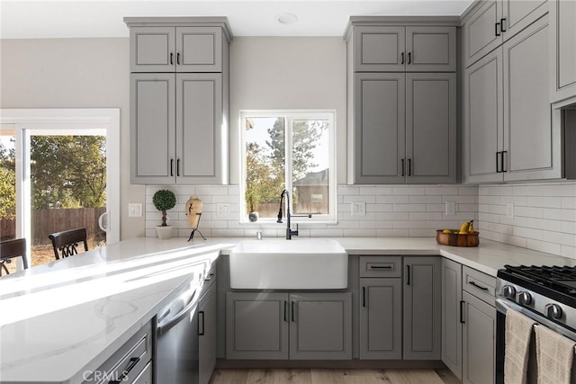 kitchen with stainless steel appliances, gray cabinets, a sink, and light stone countertops