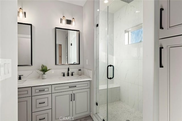 bathroom with a sink, a marble finish shower, and double vanity