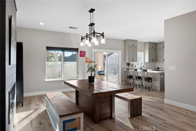 dining space featuring a fireplace, light wood finished floors, recessed lighting, visible vents, and baseboards