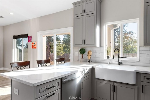 kitchen featuring dishwasher, a kitchen breakfast bar, a sink, and gray cabinetry