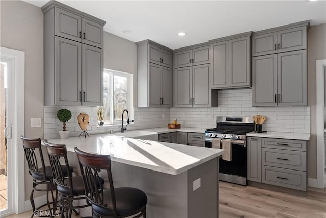 kitchen with gray cabinets, light countertops, stainless steel range with gas stovetop, a peninsula, and a kitchen breakfast bar