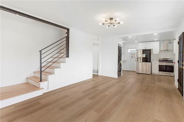 unfurnished living room with stacked washer / drying machine, light wood-style flooring, an inviting chandelier, and stairs