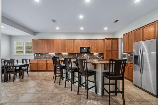40467 Tiger Way, Palmdale, CA 93551 - kitchen with brown cabinets, black microwave, a kitchen island with sink, backsplash, and stainless steel refrigerator with ice dispenser