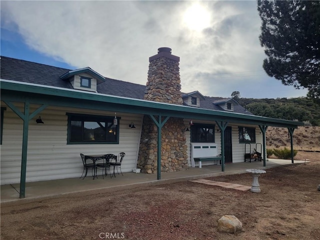 back of property with a patio area, stone siding, and roof with shingles