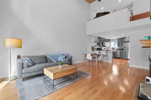 living room featuring light wood-type flooring, baseboards, and a towering ceiling