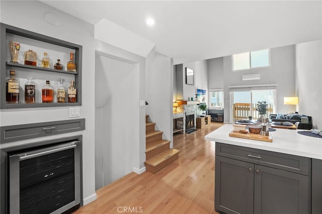 bar featuring stairs, wine cooler, light wood-style flooring, and a fireplace