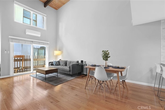 living area with high vaulted ceiling, a healthy amount of sunlight, wood finished floors, and a wall unit AC
