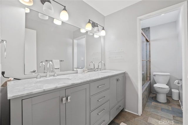 bathroom with stone tile floors, double vanity, toilet, and a sink
