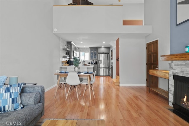 dining room with a fireplace, light wood-style floors, a towering ceiling, and baseboards
