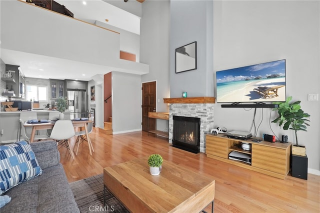 living area with a stone fireplace, baseboards, light wood-style floors, and a high ceiling