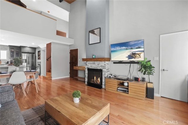 living area with light wood-type flooring, baseboards, a stone fireplace, and a towering ceiling
