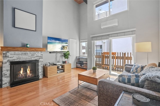 living room with a wall mounted air conditioner, a stone fireplace, wood finished floors, and a towering ceiling