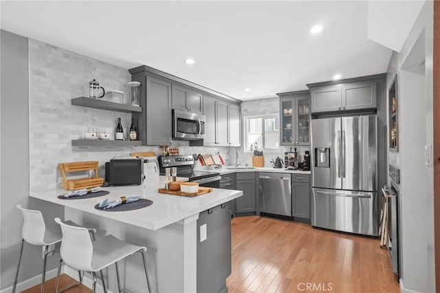 kitchen featuring open shelves, light countertops, appliances with stainless steel finishes, glass insert cabinets, and a peninsula