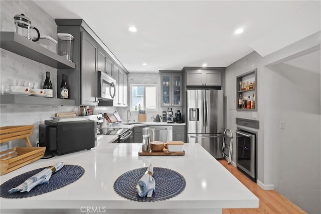 kitchen with open shelves, glass insert cabinets, gray cabinets, appliances with stainless steel finishes, and a sink