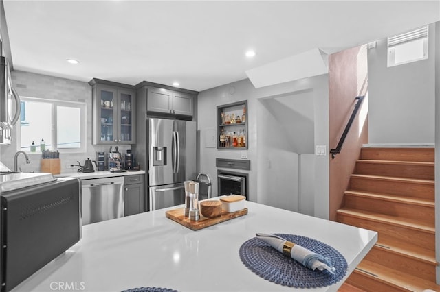 kitchen featuring gray cabinetry, glass insert cabinets, light countertops, recessed lighting, and stainless steel appliances
