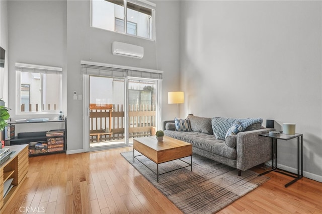 living area featuring hardwood / wood-style floors, a towering ceiling, baseboards, and a wall mounted air conditioner