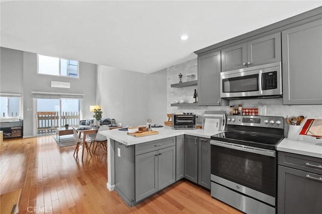 kitchen with gray cabinetry, open shelves, appliances with stainless steel finishes, a peninsula, and light countertops