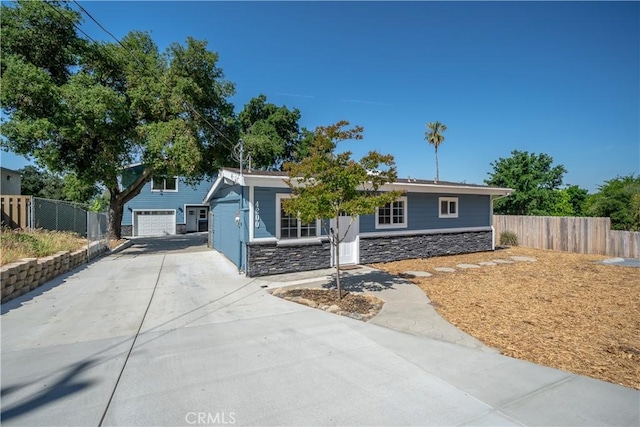 view of front facade with a garage, stone siding, concrete driveway, and fence