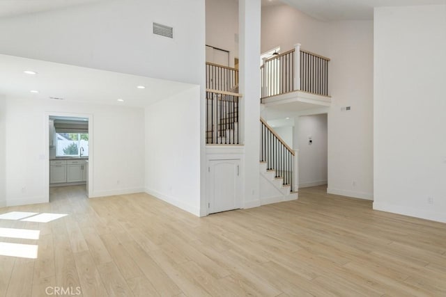 spare room featuring light wood-style flooring, a high ceiling, visible vents, baseboards, and stairs