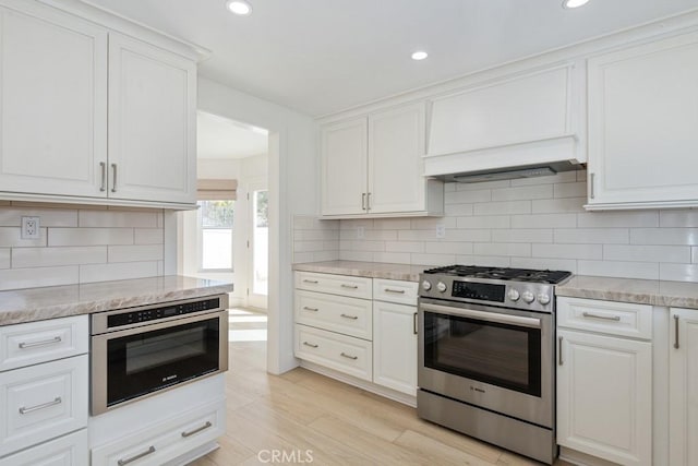 kitchen featuring light wood-style flooring, appliances with stainless steel finishes, white cabinets, and decorative backsplash