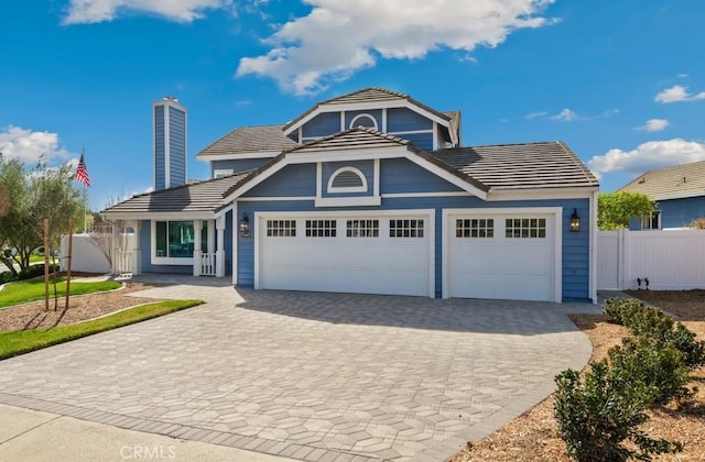 view of front of house featuring an attached garage, a tile roof, a chimney, and decorative driveway