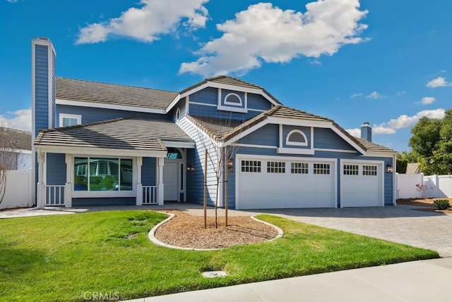 view of front facade featuring a chimney, a tiled roof, an attached garage, decorative driveway, and a front yard