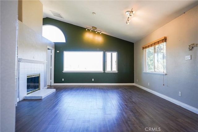 unfurnished living room featuring dark wood-style flooring, vaulted ceiling, and a tiled fireplace