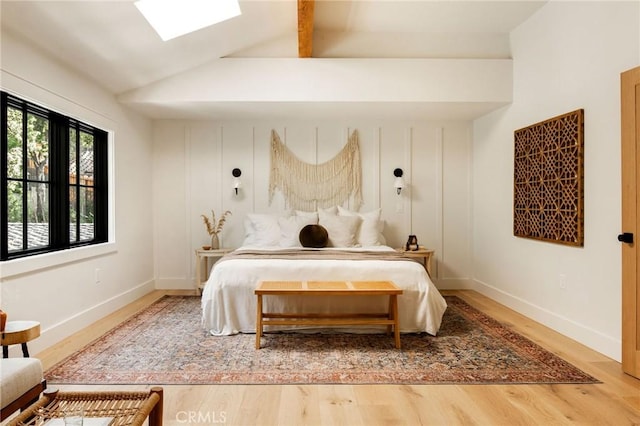 bedroom featuring lofted ceiling with skylight, baseboards, and wood finished floors