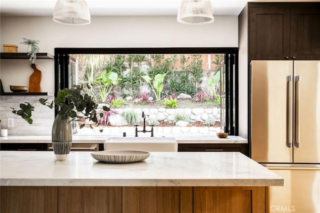 interior space with tasteful backsplash, high quality fridge, light stone countertops, open shelves, and a sink