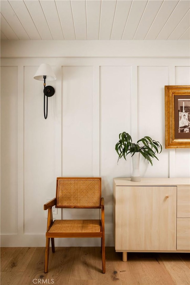 sitting room featuring light wood-type flooring, wood ceiling, and a decorative wall