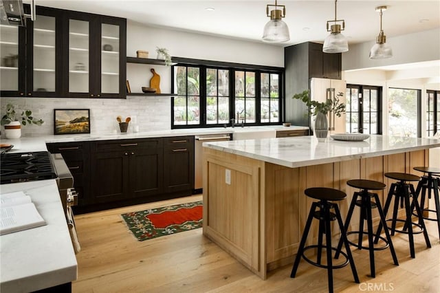 bar featuring pendant lighting, high end fridge, light wood-style flooring, stainless steel dishwasher, and plenty of natural light