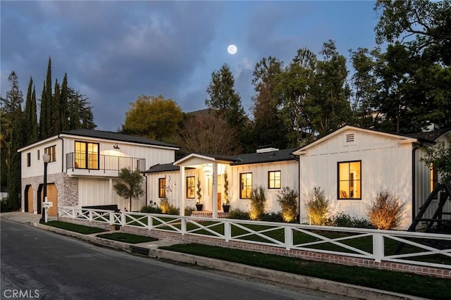 modern inspired farmhouse featuring a fenced front yard, a balcony, a garage, stone siding, and driveway