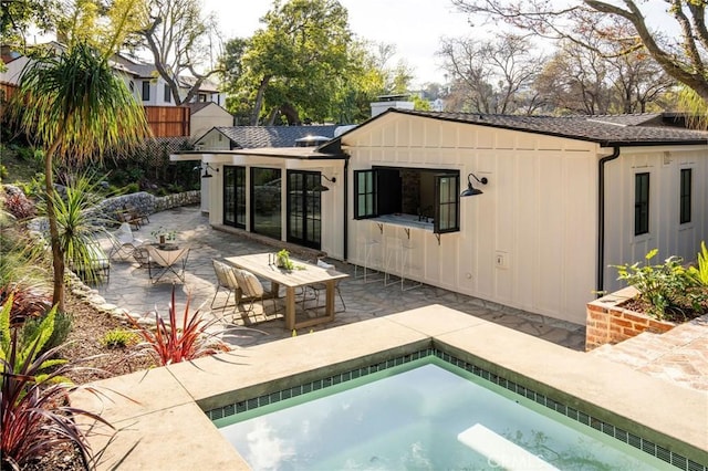 back of property featuring outdoor dining area, a chimney, a shingled roof, a hot tub, and a patio area