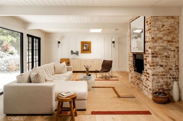 living room with wooden ceiling, a decorative wall, light wood-type flooring, a brick fireplace, and beamed ceiling