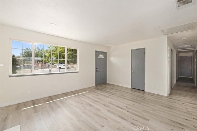 unfurnished room with attic access, light wood-type flooring, visible vents, and baseboards