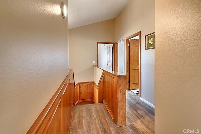 hallway featuring vaulted ceiling, an upstairs landing, wood finished floors, and a textured wall